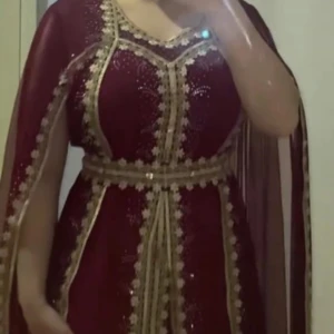 Vinröd klänning med gulddetaljer - Elegant vinröd klänning ( koftan) med vackra gulddetaljer och broderier. Klänningen har en lång design och är dekorerad med glittrande paljetter. Perfekt för speciella tillfällen. 36-40 i stl.