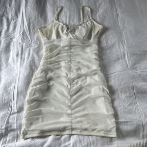 Vit klänning från Divided - Säljer en stilren vit klänning från Divided. Den har smala axelband och en åtsittande passform med rynkade detaljer framtill. Perfekt för en somrig look! Har några fläckar med det går lätt bort i tvätten !OBS No free shipping , går ej att ta bort 