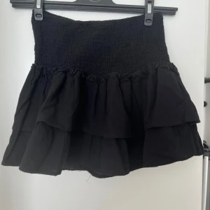 Svart volangkjol - Snygg svart kortkjol med volanger. Perfekt för en trendig look. Den har en elastisk midja för bekväm passform.