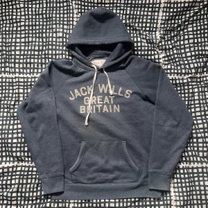 Skitsnygg hoodie - Säljer en snygg mörkblå hoodie. med texten 'Jack Wills Great Britain' på framsidan. Tröjan har en klassisk känguruficka och justerbar huva med snören. Perfekt för en avslappnad stil!
