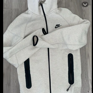 Vit hoodie från Nike - Säljer en stilren vit hoodie från Nike med dragkedja och svarta detaljer. Den har en justerbar huva och två praktiska fickor med dragkedjor. Perfekt för en avslappnad look. Den är storlek 158-170.