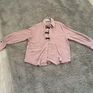 Rosa blus/skjorta💓 - Charmig rosa blus/skjorta och svarta små rosetter framtill som har använts 1 gång innan. Den har långa ärmar med knappar vid ärmsluten och en klassisk krage. Perfekt för en söt och stilren look. Storleken är i L men passar även i M💓💓