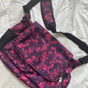 Färgglad axelväska med mönster - Snygg axelväska med ett unikt och färgglatt mönster i rosa och lila nyanser. Väskan har en justerbar axelrem och flera praktiska fack med dragkedja för enkel förvaring. Perfekt för att liva upp din outfit!