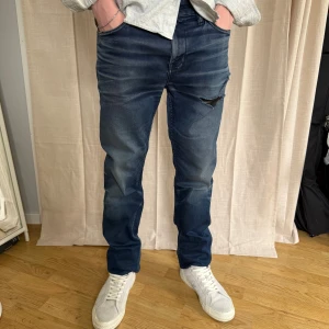 Blå jeansbyxor från Hugo Boss - Snygga blå jeansbyxor från Hugo Boss med en cool slitning på låret. De har en klassisk femficksdesign och en knappgylf. Perfekta för en avslappnad stil.