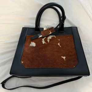 Svart och brun handväska med pälsdetaljer - Snygg handväska i svart och brun med unika fuskpälsdetaljer på framsidan