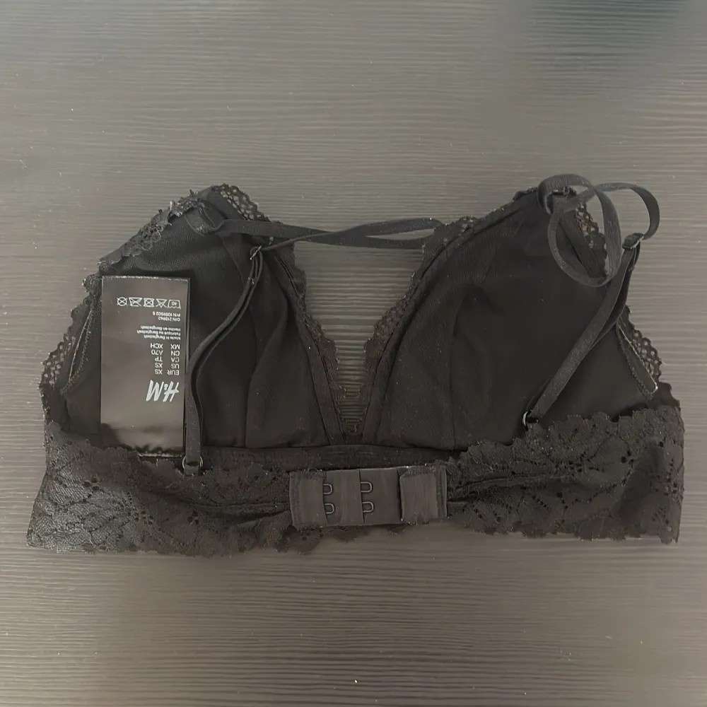 Snygg svart spets bralette från H&M med justerbara axelband och hakknäppning bak. Perfekt för en stilren och bekväm look. Spetsdetaljerna ger en elegant touch.. Muu.