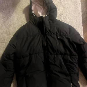 Svart dunjacka från Bershka - Säljer en svart dunjacka från Bershka med huva och dragkedja. Perfekt för kyliga dagar. Jackan har en stilren design och är både varm och bekväm.