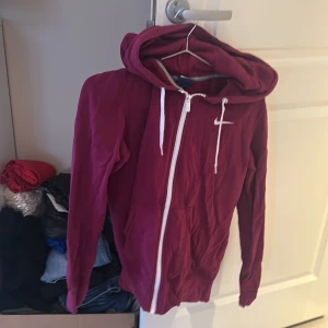 Lila hoodie från Nike - Säljer en snygg vinröd hoodie från Nike med dragkedja och huva. Perfekt för en avslappnad stil. Den har en klassisk Nike-logga på bröstet och vita snören vid huvan.