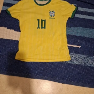 Gul Brasilien fotbollströja med pele nmr 10 2016 - Säljer en gul Brasilien fotbollströja med nummer 10 och CBF-logga på bröstet. Tröjan har korta ärmar och gröna detaljer vid krage och ärmslut. Perfekt för fotbollsfans!