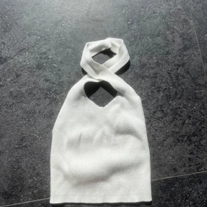 Vit ribbad halterneck topp - Snygg vit ribbad halterneck topp med korsad design vid halsen. Perfekt för en stilren och modern look. Passar bra till både jeans och kjol.