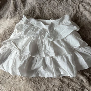 Vit volangkjol - Charmig vit kortkjol med flera lager av volanger som ger en lekfull look. Perfekt till sommaren🩷