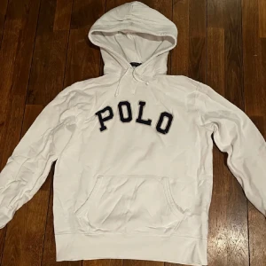 Vit hoodie från Polo - Säljer en stilren vit hoodie från Polo med stor logotyp på bröstet. Tröjan har en klassisk känguruficka och justerbar huva. Perfekt för en avslappnad stil.