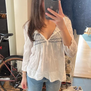 Vit blus  - Säljer en jättesöt blus med broderade detaljer. Man kan välja att knyta snörena eller ha som på bilden. Blusen har inga defekter. Här av dig för frågor eller fler bilder!