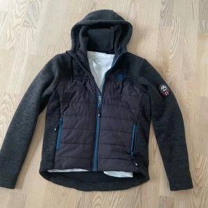 Grå cardigan - Säljer en grå/blå cardigan i väldigt bra skick, den är knappt använd och har inga defekter. Den är i storlek XS, perfekt för våren. Märke: Scandinavian Explorer. Nypris:1500kr