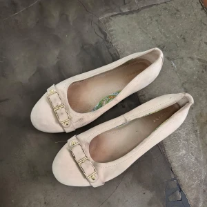 Beige ballerinaskor med spänne - Säljer ett par eleganta beige ballerinaskor från Depeche. Skorna har ett dekorativt spänne framtill och är tillverkade i syntetmaterial. Perfekta för en stilren look.