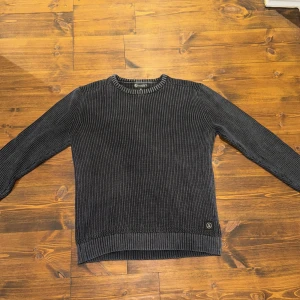 Stickad tröja från Lagency - Säljer en snygg stickad tröja från Lagency. Tröjan har en ribbad rund hals och långa ärmar. Perfekt för kyligare dagar. Lagency-logga vid nederkanten ger en stilren touch. Köpt från Thernlunds men inte använd mycket då den tyvärr var för stor.
