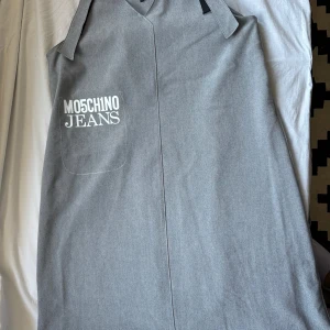 Grå klänning från Moschino Jeans - Snygg grå klänning från Moschino Jeans med en stilren design. Klänningen har en enkel passform och ett tryck med märkesnamnet på framsidan. Perfekt för en minimalistisk look.