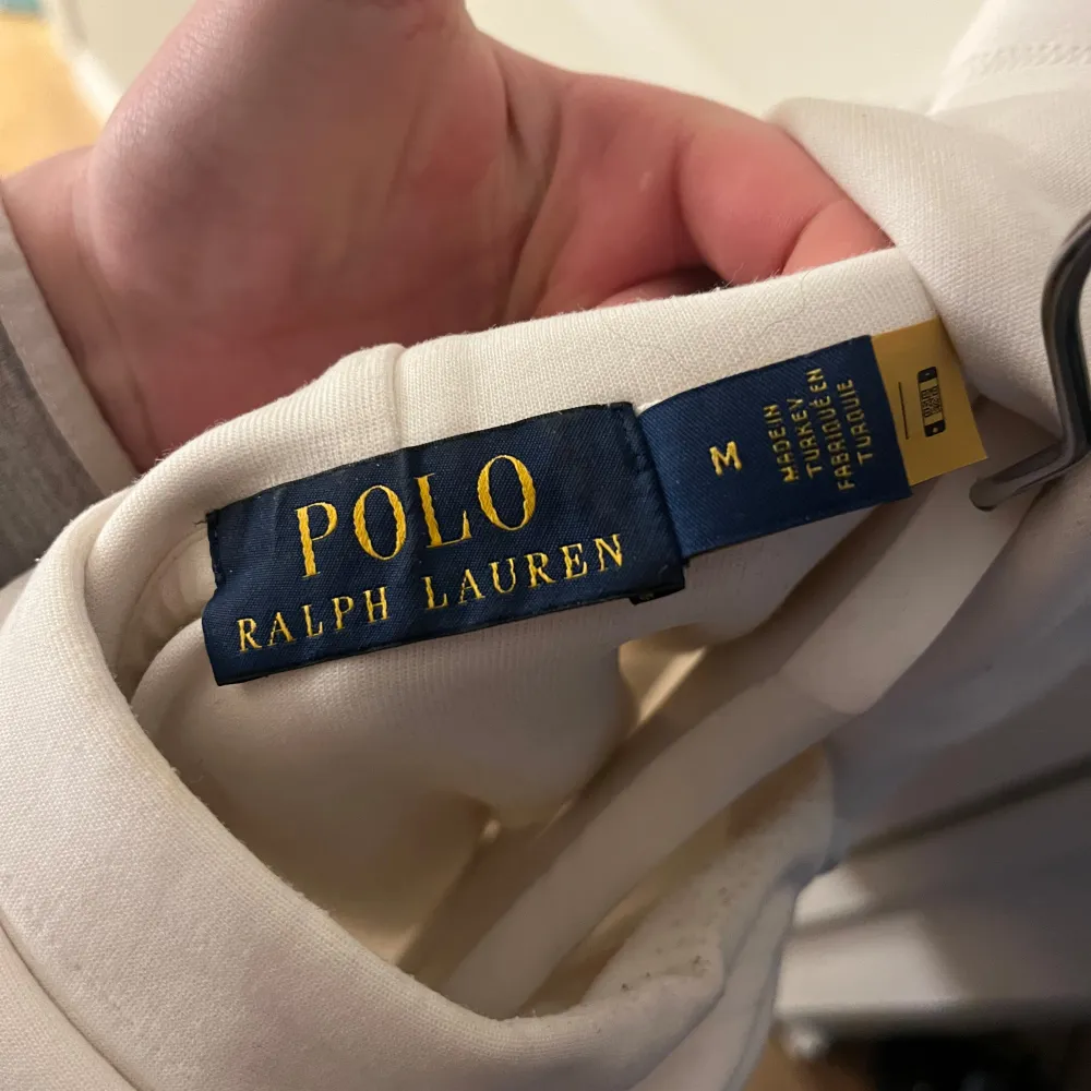 Säljer en stilren vit hoodie från Polo Ralph Lauren med det klassiska logotypbroderiet på bröstet. Tröjan har en känguruficka och justerbar huva med snören. Perfekt för en avslappnad look.. Neuletakit & Villapaidat.
