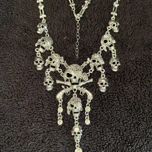 Halsband med dödskallar i silver - Unikt halsband i silver med flera detaljerade dödskallar och korsade ben. Perfekt för att ge en edgy touch till din stil. Kedjan är justerbar för att passa olika längder.
