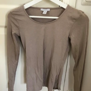 Beige långärmad topp från Amisu - Säljer en stilren beige långärmad topp från Amisu. Perfekt för en enkel och elegant look. Toppen har en rund halsringning och är tillverkad i ett mjukt material.