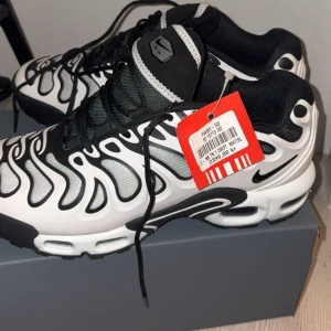 Nike TN air sneakers i svart och vitt - Snygga Nike Air sneakers med ett unikt svartvitt mönster och klassisk snörning. Skorna har en modern design med vågformade detaljer och en bekväm sula för extra komfort. Perfekta för en stilren look.