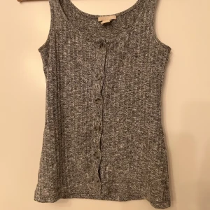 Grå ribbad linnetopp med knappar - Snygg grå-melerad ribbad linnetopp med knappar framtill. Perfekt för en avslappnad stil. Ärmlös och har en bekväm passform. Bra skick!