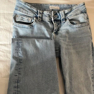 Ljusblå jeans med bootcut - Snygga ljusblå lowwaist jeans med bootcut-stil och klassisk femficksdesign. De har en dragkedja och knapp framtill samt dekorativa bakfickor med knappar.