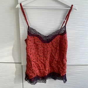 Linne med spets från Odd Molly - Säljer ett orange linne från Odd Molly med små hjärtan och vacker spetsdetalj. Linnet har justerbara axelband och en söt knappdetalj framtill. Perfekt för en romantisk look! 💖Använd fåtal gånger. 