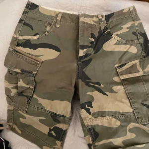 Camouflage shorts från Jack & Jones - Säljer ett par coola camouflage shorts från Jack & Jones. De har en avslappnad passform med flera praktiska fickor och knappar. Perfekta för en casual look. Passar bra för sommarens äventyr!