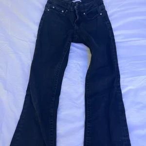 Svarta bootcut jeans - Snygga svarta bootcut jeans med låg midja och klassisk femficksdesign. Jeansen har en dragkedja och knappar framtill samt stiliga bakfickor med lock och knapp. Perfekta för en trendig look! Skriv för köpa eller frågor💗