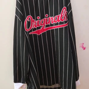 Svart och vit randig tröja med text - Säljer en svart och vit randig tröja med texten 'Originals' i rött på framsidan. Tröjan har långa ärmar och en vit krage. Perfekt för en avslappnad stil.