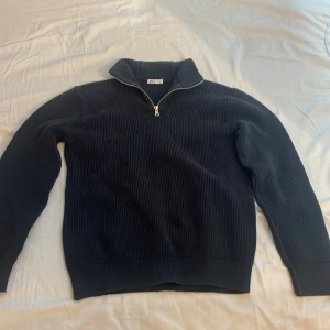 Svart ribbad tröja med dragkedja - Snygg svart ribbad tröja med dragkedja i halsen. Perfekt för kyligare dagar med sin stilrena design och bekväma passform. Tröjan har långa ärmar och en hög krage som ger extra värme.