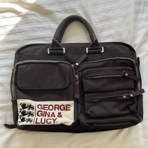 George Gina Lucy Datorväska - I bra skick och har många olika fack. Mått: 43 x 30 cm. Bredd = 8 - 12 cm. Man kan sätta fast en axelrem om man vill. Enda defekten är att dragkedjan på undersidan som gör att man kan göra väskan bredare har fastnat lite, men det går fortfarande att justera bredden med den. 