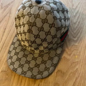 Mönstrad keps från Gucci - Snygg keps från Gucci med det ikoniska mönstret i brunt och beige. Kepsen har en justerbar rem baktill och en klassisk skärm framtill. Perfekt för att ge din outfit en lyxig touch. Denna keps är i storlek medium, möts up i Solna✌️✌️