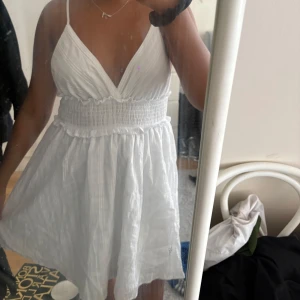 Vit kort sommarklänning med smock - Supersöt vit kort klänning med smala axelband och v-ringning. Är endast använd ett fåtal gånger men är så fin💞