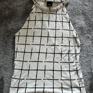 Beige rutig linnetopp från Gina Tricot - Snygg beige linnetopp från Gina Tricot med svart rutigt mönster. Toppen är ärmlös med hög halsringning och har en rak, avslappnad passform. Perfekt för varma dagar eller att styla lager på lager.