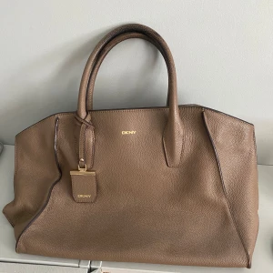 Brun handväska från DKNY i skinn - Snygg och rymlig brun handväska från DKNY i äkta skinn. Stilren väska som passar till skolan eller vardag 