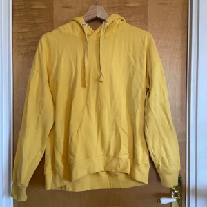 Gul hoodie från lager157 med huva - Gul hoodie från 157 med klassisk huva och snörning. Tröjan har ribbade muddar vid ärmslut och nederkant, samt en relaxed passform. Perfekt för dig som gillar en enkel och färgglad stil. Materialet är mjuk bomull som känns skönt mot huden. Den är även ganska tunn så skönt att ha under sommar eller höst. 