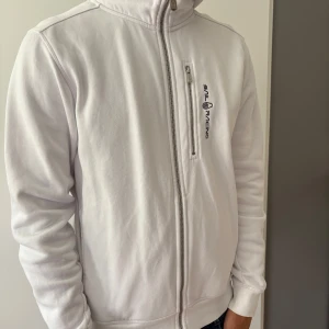 Vit hoodiejacka från Sail Racing - Säljer min riktigt snygga Sail racing luvtröja eftersom den inte används. Vit hoodiejacka från Sail Racing med dragkedja framtill och bröstficka.  Storlek M och ser ny ut! 