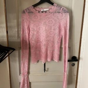 Rosa spetsblus från Zara - Supersöt rosa spetsblus från Zara med långärmad design och volangdetaljer vid ärmslut och halsringning. Blusen är genomskinlig och har ett fint mönster i spets, perfekt för dig som gillar en feminin och trendig stil.