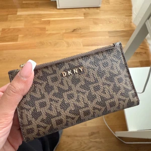 Brun DKNY plånbok med logomönster - Pris: 500kr.  Kvitto finns