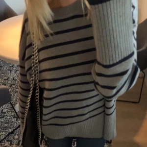 Randig grå stickad tröja från Zara - Supermysig stickad tröja från Zara i grått med mörkblå ränder. Oversized fit med breda ribbade muddar vid ärmslut och nederkant. Perfekt till jeans och sneakers för en chill look. Rund halsringning och långärmad modell.