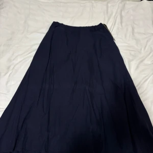 Mörkblå långkjol i bomull - Enkel och stilren mörkblå långkjol i mjukt bomullstyg. Kjolen har en lätt utställd form och resår i midjan för skön passform. Perfekt att matcha med en crop top eller stickad tröja för en chill look.