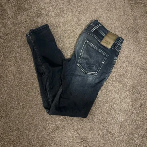 Replay Anbass slim jeans mörkblå 29/32 - Snygga Replay Anbass jeans i mörkblå tvätt med slitningar och klassiska fem fickor. Slim fit-modell med normal midja och dragkedjegylf. Jeansen har vita kontrastsömmar och Replay-logga på bakfickan. Perfekta för en stilren och avslappnad look.