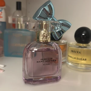 Perfect Elixir parfym från Marc Jacobs - Säljer en elegant parfymflaska från Marc Jacobs, Perfect Elixir. Flaskan är lila med en unik kork prydd med en stor, blå rosett. Innehåller 30 ml Eau de Parfum. Perfekt för den som älskar en lyxig och stilren doft. Pris kan diskuteras 