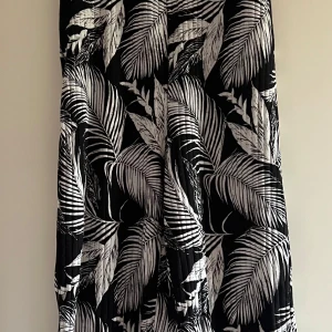 Svartvit långkjol med bladprint - Snygg svart jumpsuit med vita bladmönster. Jumpsuit en  har plisserad struktur och ett riktigt flowy fall. Perfekt för dig som gillar statement-plagg med tropisk vibe. Resår i midjan för skön passform.