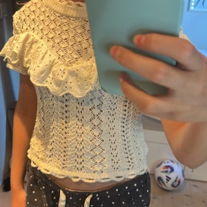 Vit virkad topp med volang från Zara - Superfin vit virkad top från Zara med korta ärmar och en volang med broderade detaljer. Tröjan har ett genombrutet mönster och ribbad kant vid hals och nederdel. 