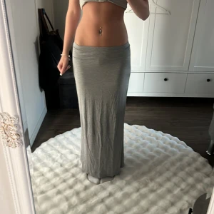 Grå långkjol i mjukt material - Säljer en enkel och stilren grå långkjol med rak passform. Kjolen är i ett mjukt och stretchigt material som sitter skönt i midjan. Perfekt att styla med crop top eller hoodie för en chill vibe. Passar dig som gillar minimalistisk look.