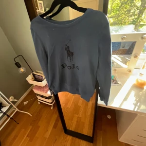 Blå långärmad tröja från Polo Ralph Lauren - Snygg blå långärmad tröja från Polo Ralph Lauren med klassisk logga framtill. Tröjan har en avslappnad passform och är perfekt för dig som gillar stilrena och bekväma plagg. Passar till jeans eller mjukisbyxor för en chill look. Strl 12-14