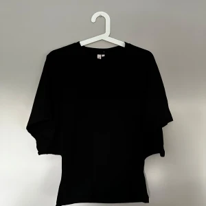 Svart loose topp med vida ärmar - En svart topp med loose passform och extra vida, nästan fladdermusliknande ärmar. Toppen har rund halsringning och är tillverkad i ett mjukt material som känns skönt mot huden. Perfekt för dig som gillar en avslappnad och trendig stil.